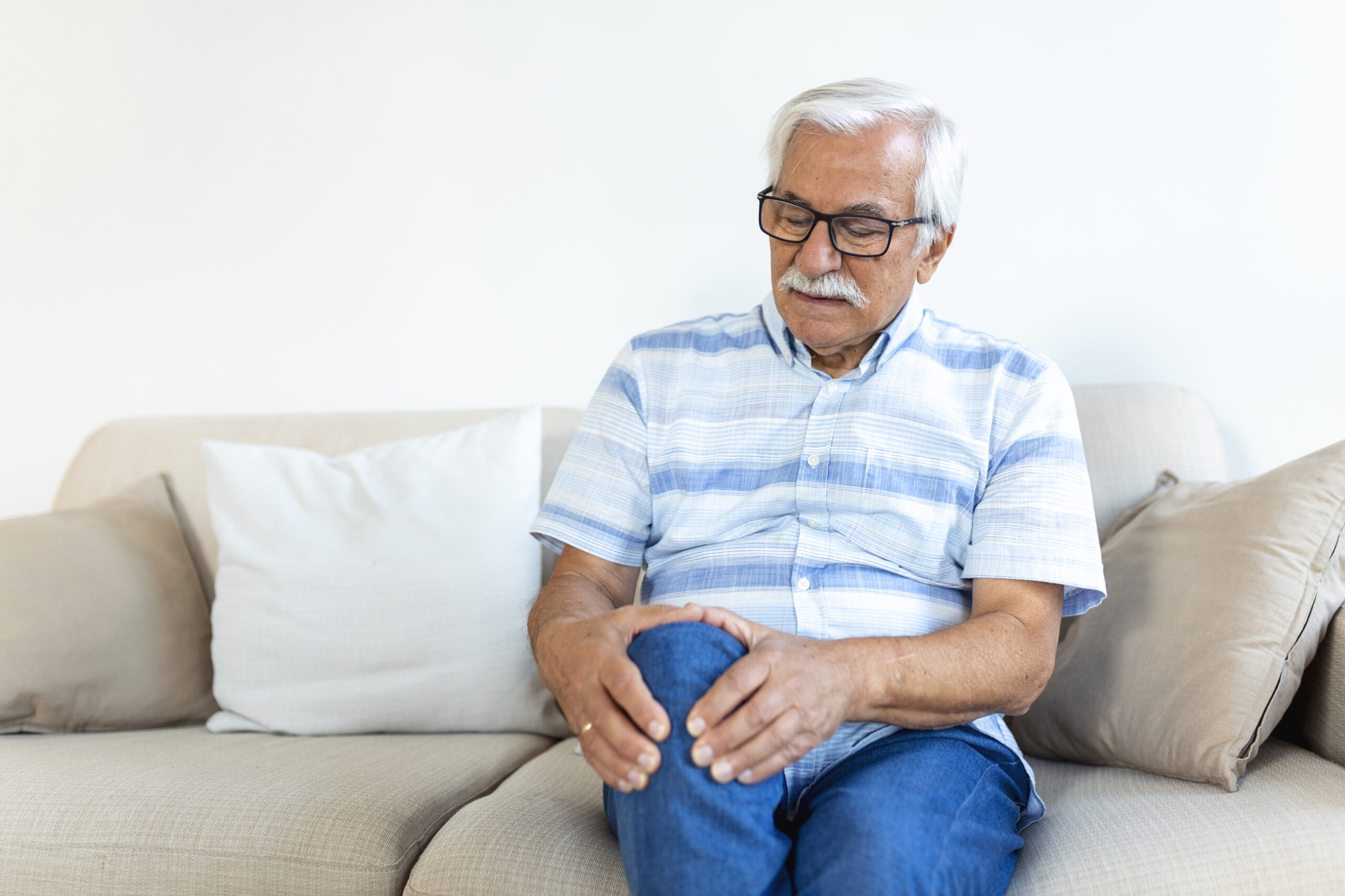 Homem idoso com dor nos ossos devido à osteoporose sentado no sofá